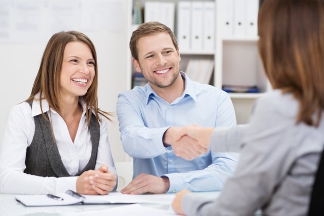 Smiling young man shaking hands with an insurance agent or investment adviser as he sits in a meeting with his wife in her office Smiling young man shaking hands with an insurance agent or investment adviser as he sits in a meeting with his wife in her office